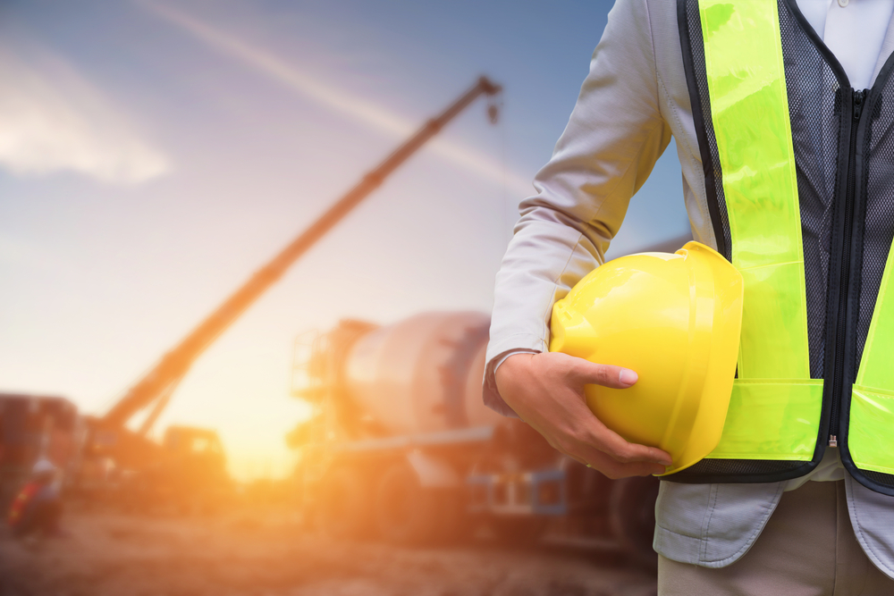 Construction worker holding a hard hat on site at sunset