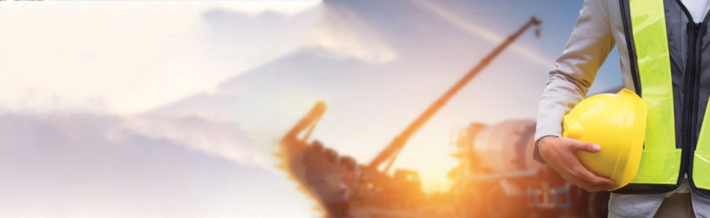 Construction worker holding a hard hat with a crane at sunset