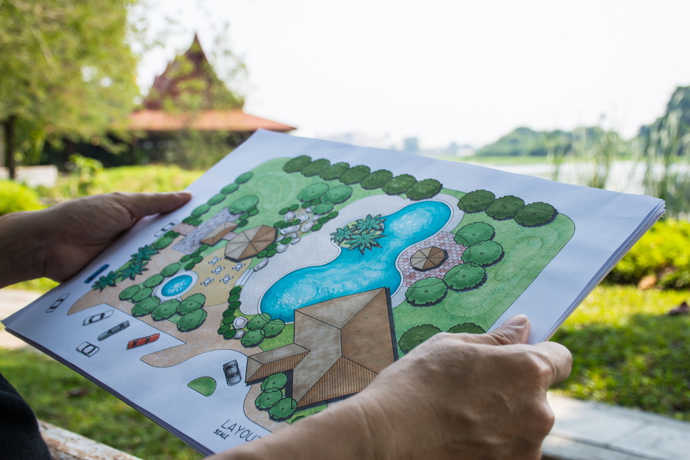 Landscape design plan held in front of a garden