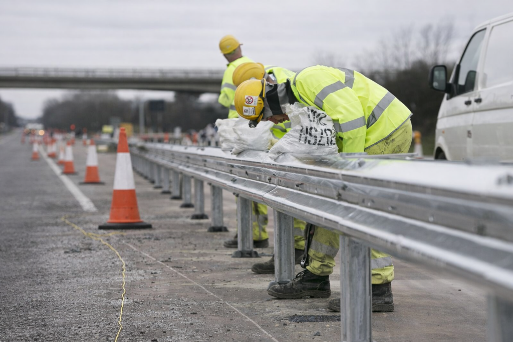 Highway maintenance workers repairing a crash barrier beside traffic cones
