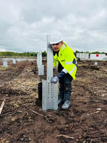 Labour worker in hard hat installing solar mounting posts on a solar farm